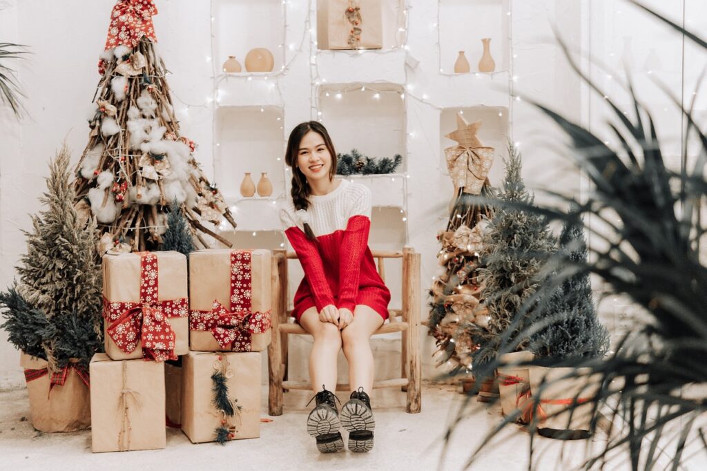 a young lady sitting beside a christmas tree and presents